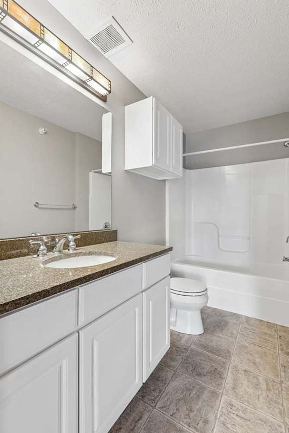 Apartment bathroom with a single-sink vanity, large mirror, toilet, and a tub/shower combination with neutral finishes and durable flooring.