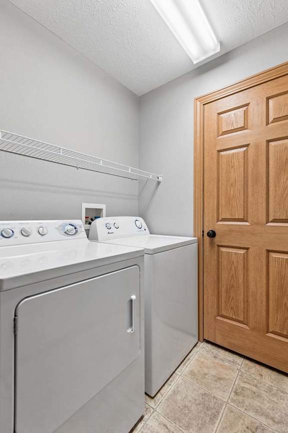 Apartment laundry room with a full-size washer and dryer, upper wire shelf for storage, durable flooring, and a wood-trimmed utility closet door.