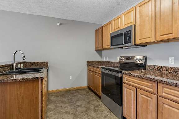 Modern kitchen featuring granite counters, wood cabinets, and stainless steel appliances.