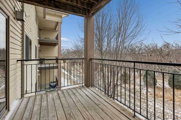 Private apartment balcony with wood decking, metal railing, and views of mature trees, offering an outdoor space accessible from the apartment.