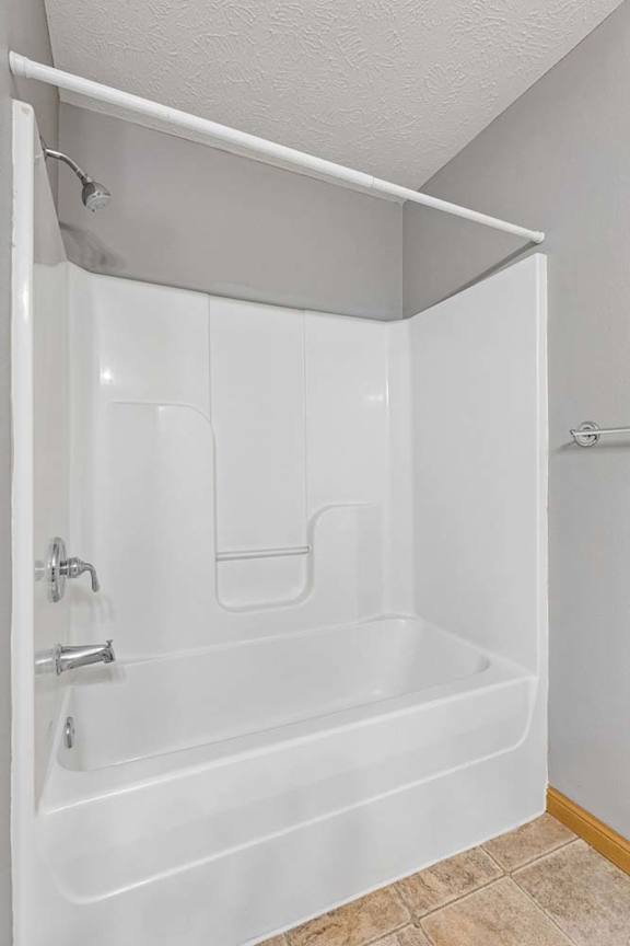 Apartment bathroom with a white tub and shower combination, built-in surround, and a shower curtain rod, featuring a clean, neutral design.