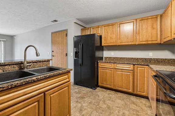 Apartment kitchen with wood cabinets, black appliances, laminate countertops, and a center island with a sink, offering an open layout to the living area.