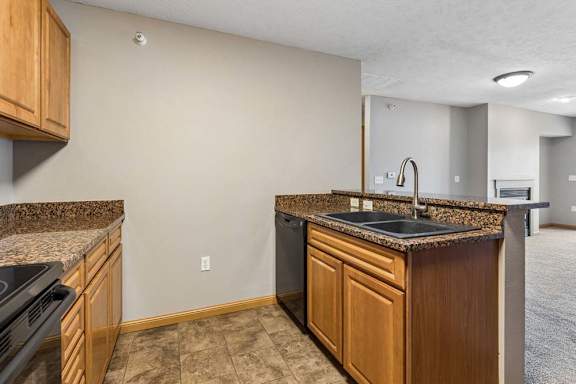 Open apartment kitchen with wood cabinets, laminate countertops, a breakfast bar, black appliances, and a sink overlooking the adjacent living area.