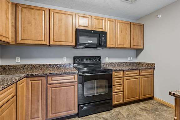 Apartment kitchen with wood cabinets, laminate countertops, black oven and microwave, and ample upper and lower cabinet storage.