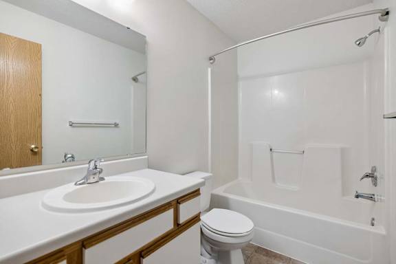 Bright apartment bathroom with a large vanity mirror, single sink, white tub and shower surround, and neutral finishes.