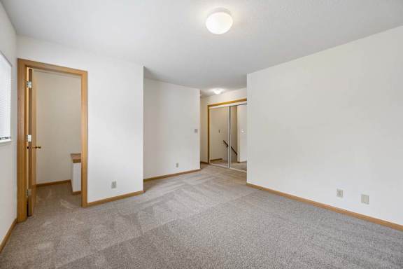 Carpeted bedroom with mirrored closet doors, a side window, and an open doorway leading to an adjacent interior space.