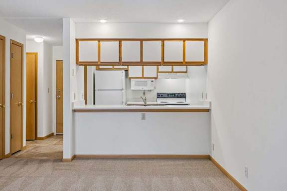 Open kitchen with a breakfast bar, white appliances, wood-trimmed cabinetry, and recessed lighting beside the living area.