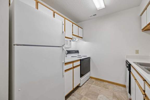 Galley-style kitchen with white cabinets, full-size appliances, double sink, dishwasher, and tile flooring.