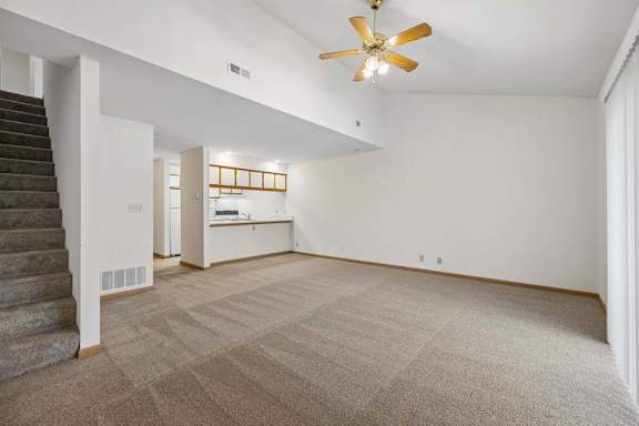 Open living room with vaulted ceiling and ceiling fan, carpeted staircase, and a breakfast bar connecting to the kitchen.