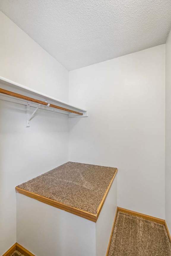 Walk-in apartment closet with a hanging rod, upper shelf, neutral walls, and a built-in storage ledge for added organization.