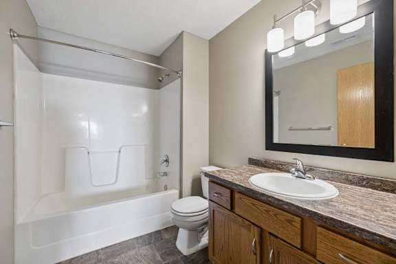 Full bathroom with a tub-shower combination, wood vanity, stone-look countertop, framed mirror, and modern vanity lighting.