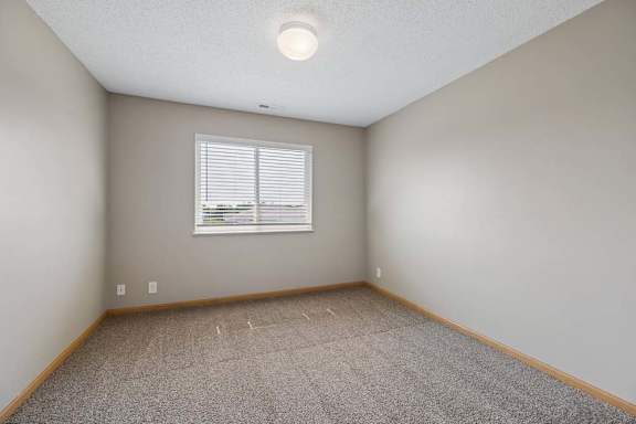 Sunlit bedroom with wall-to-wall carpeting and a window with blinds, offering open space for flexible furniture placement.