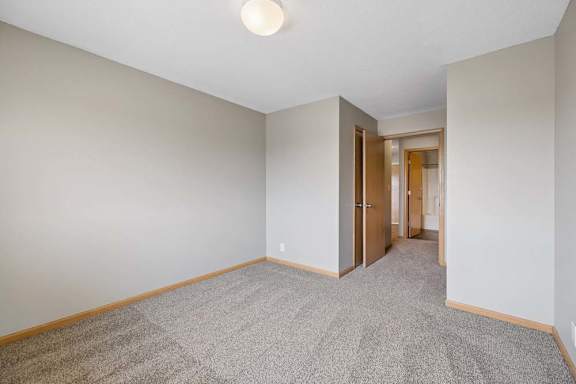 Unfurnished bedroom with soft carpeting, an angled entryway, and open doors connecting to the hall and nearby bathroom.