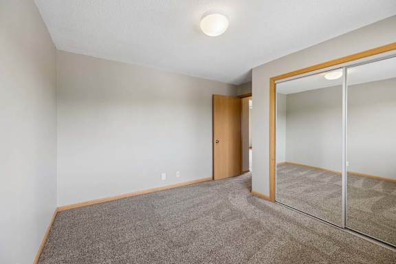 Bedroom with wall-to-wall carpeting and large mirrored closet doors that reflect the open layout and overhead lighting.