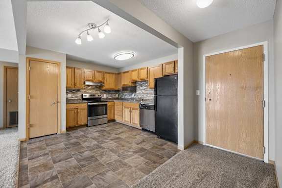 Apartment entry opens to an updated kitchen with oak cabinetry, mosaic backsplash, patterned flooring, and full-size appliances.