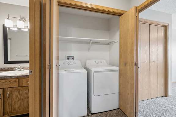 Laundry closet with full-size washer and dryer, overhead shelving, and convenient placement beside the bathroom and bedroom.