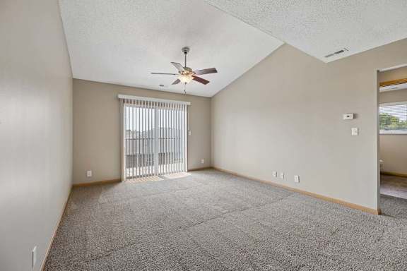 Vaulted living room with a ceiling fan, sliding glass door to the balcony, and an open doorway to an adjoining room.