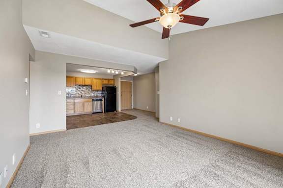 Vaulted living room with a ceiling fan and open sightline to the kitchen, featuring oak cabinetry and contrasting appliances.
