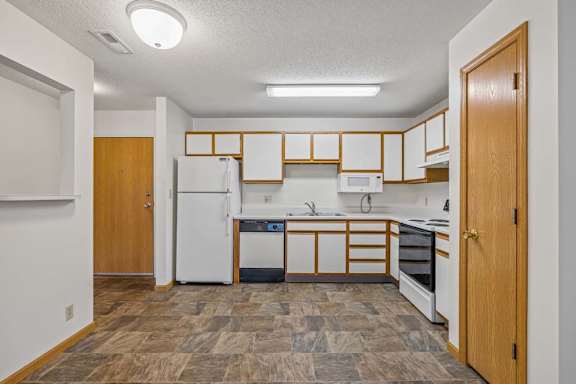 Open apartment kitchen with white cabinets, white appliances, durable flooring, and a pass-through breakfast bar connecting to the adjacent living area.