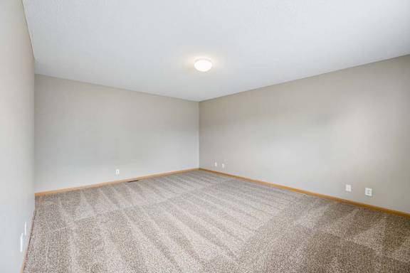 Spacious apartment bedroom with carpeted flooring, neutral walls, and a large window providing natural light.