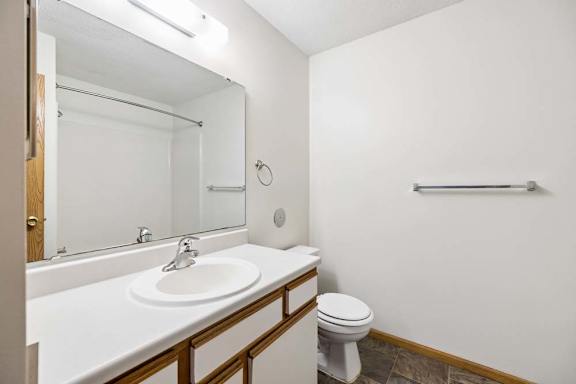 Apartment bathroom with a single-sink vanity, white and wood-tone cabinetry, a large mirror with overhead lighting, and a tub-shower combination with a towel bar.