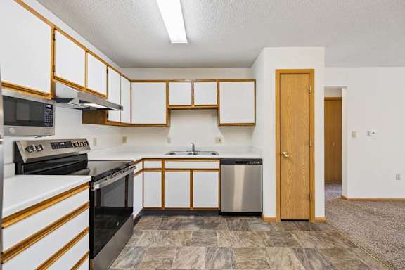 Apartment kitchen with white and wood-tone cabinetry, laminate countertops, stainless steel dishwasher, black oven, and a functional U-shaped layout open to the adjacent living area.
