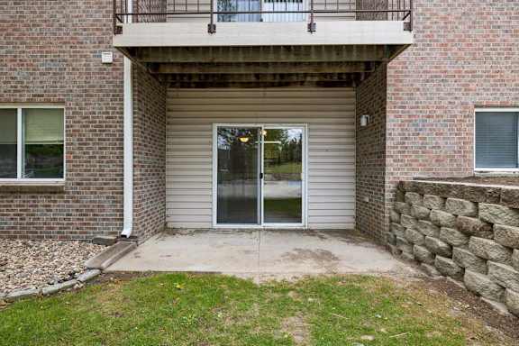 Covered ground-floor apartment patio with a concrete surface, a large sliding glass door, brick and siding exterior, and direct access to a landscaped lawn.