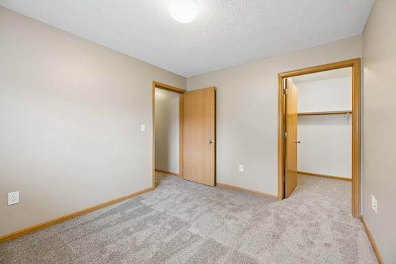 Carpeted bedroom with beige walls, an open closet with hanging storage, and a doorway leading to the hall.