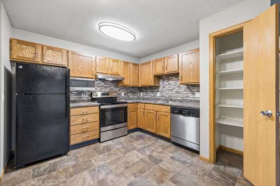 Updated kitchen with oak cabinetry, mosaic backsplash, black and stainless appliances, patterned flooring, and a shelved pantry.