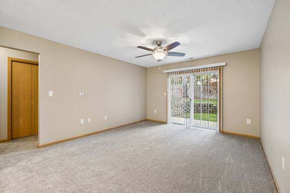 Living room with a ceiling fan and sliding glass door opening to a ground-level patio and landscaped green space.