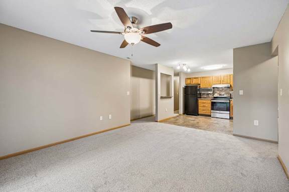 Open-concept living and dining area with a ceiling fan, carpeted flooring, and an updated kitchen visible beyond.