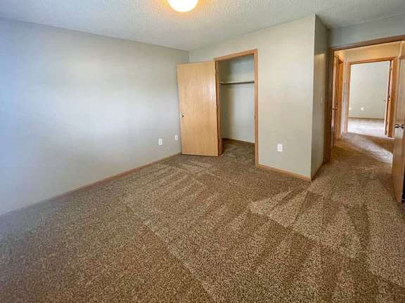A carpeted bedroom with a closet door and a window.