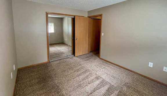 A bedroom with a carpeted floor and closet with a sliding mirrored door.