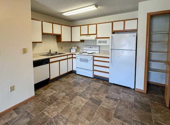 A kitchen with white appliances, a pantry closet, and white cabinets with oak trim.