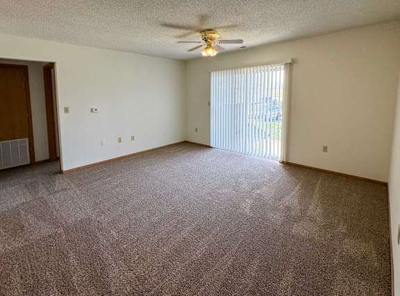 A living room with a ceiling fan, carpeted floor, and sliding glass door to a patio.
