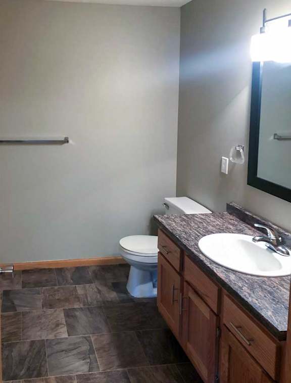 A bathroom with a granite vanity sink, and framed mirror with overhead lighting.