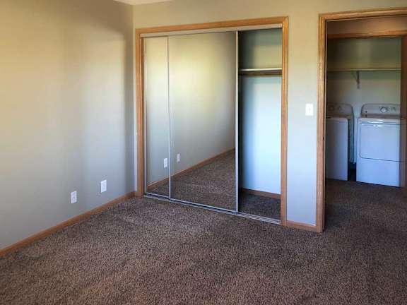 A bedroom with a carpeted floor, a sliding mirror door closet, and a door open to the hallway with a view of the laundry room.