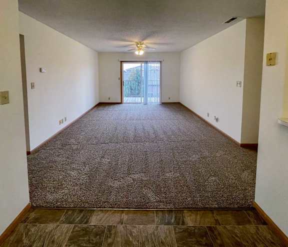 A living room with carpeted flooring, a ceiling fan, and a sliding glass door to a balcony.