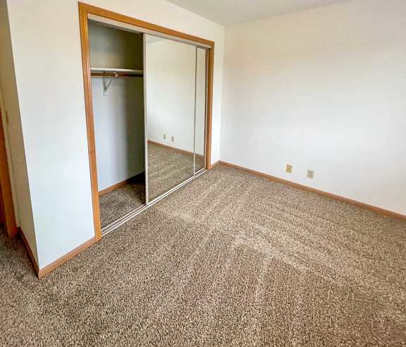 A bedroom with a carpeted floor and a sliding mirror door closet.