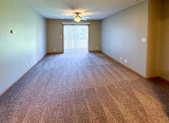 A living room with a carpeted floor, sliding glass door to a balcony, and a ceiling fan.
