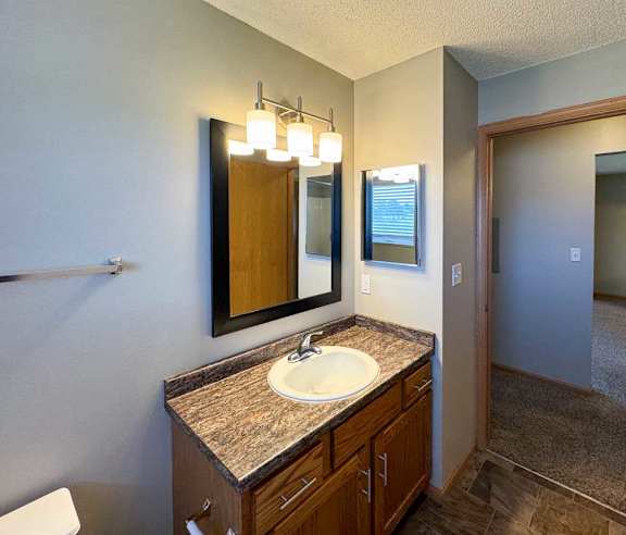 A bathroom with a granite vanity sink, mirror, medicine cabinet, and overhead lighting.