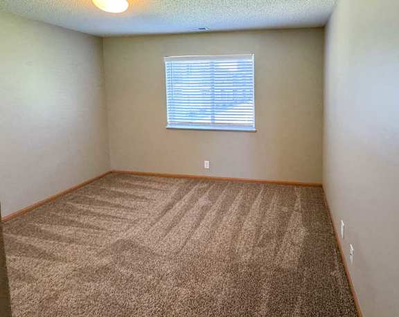 A bedroom with a carpeted floor and a window with blinds.