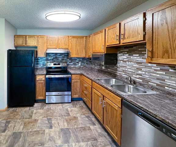 An updated kitchen with wooden cabinets, black and stainless steel appliances, granite countertops, and a tile backsplash.