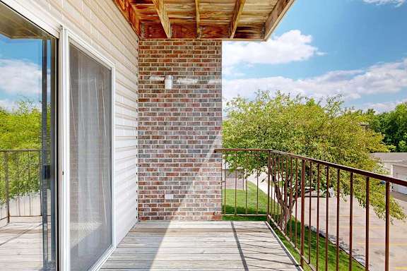 a balcony corner view with brick siding and metal railing