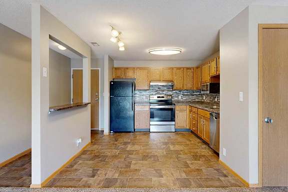 a kitchen with wooden cabinets, upgraded appliances, tile backsplash, and a windowed accent wall by the front entry