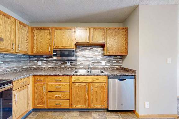 a kitchen with stainless steel dishwasher and microwave, a tile backsplash, and wooden cabinets