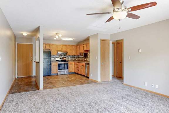 a carpeted living room with ceiling fan and open view into the kitchen