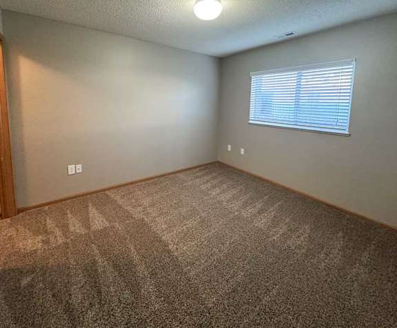A bedroom with a carpeted floor and a window with blinds.