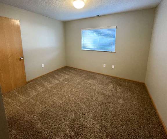 A bedroom with a carpeted floor and a window with blinds.