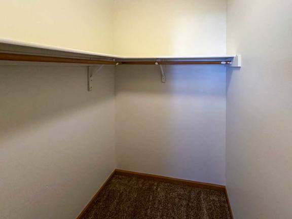 A walk-in closet with a built in overhead shelf and hanging space.